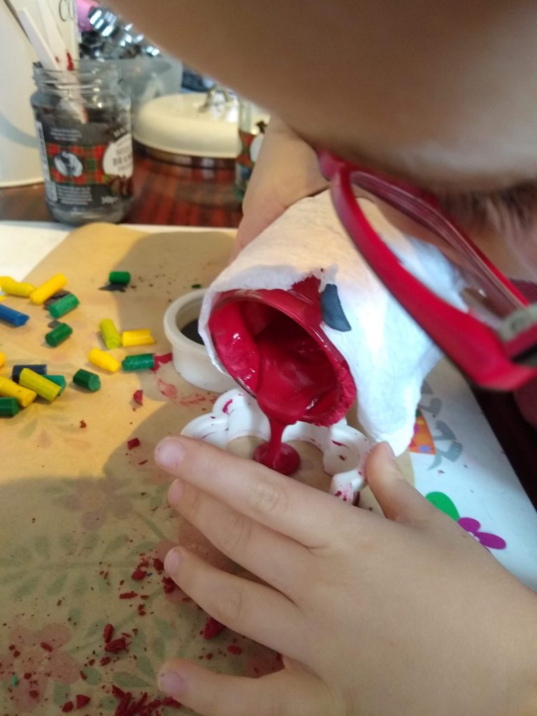 The photo shows red, melted wax crayons being poured into a flower mould.