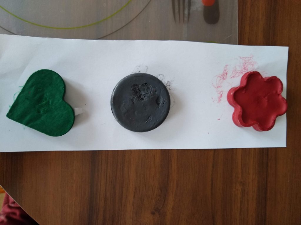 The photo shows a red, flower crayon; a grey, circle crayon; and a green, heart crayon.