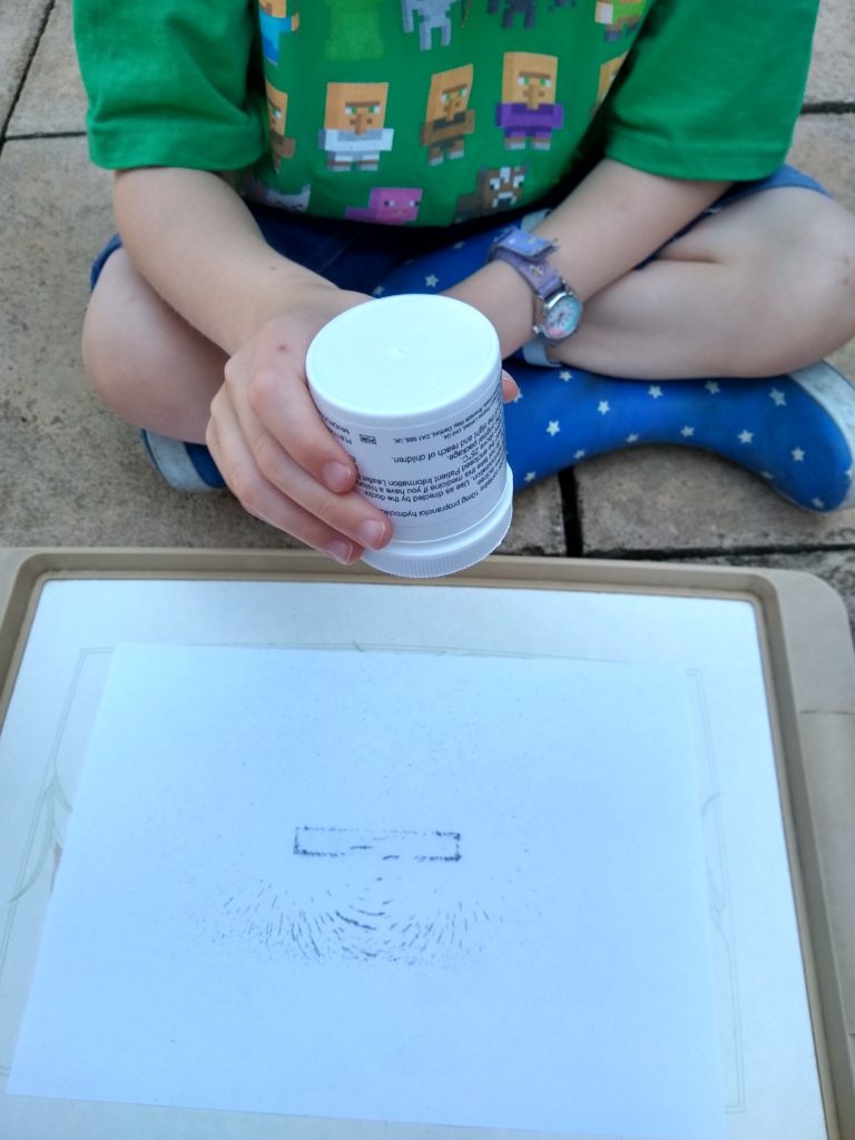 A photo of me shaking iron filings around a magnet with a piece of paper on top.