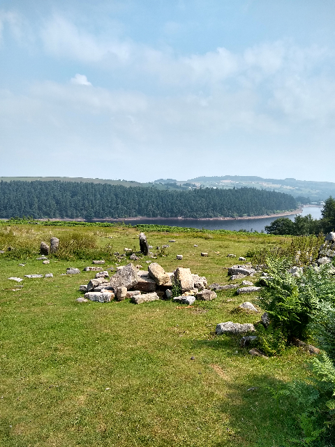 A pile of stones in the grass with a background of the reservoir.