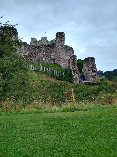 A photo showing the entrance to Conisbrough Castle; the ruined stone walls can be seen in the foreground, while the main tower can just be seen poking out over the top.