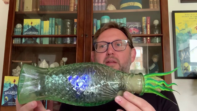 The author, Thomas Taylor, holding a fish-shaped bottle made of green glass.