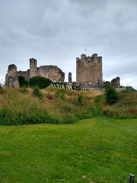 A photo of the main tower and ruined stone walls of Conisbrough Castle. There is a grass bank in the foreground.