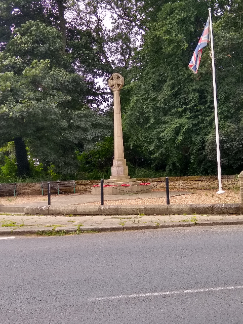 A photo of a stone monument with a cross at the top and the union jack flying to the right.